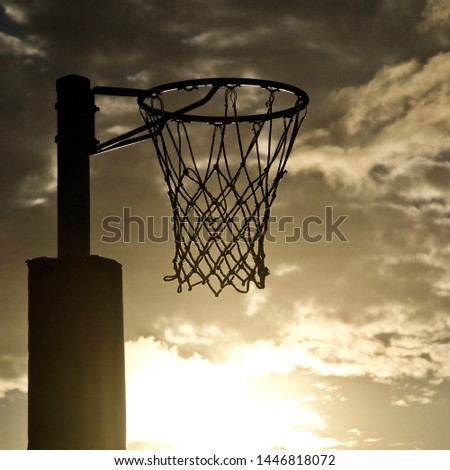 Netball Goal. Positioned left of frame, the silhouette of a Netball Goal. The setting sun casts an iridescent glow from the bottom of frame.
