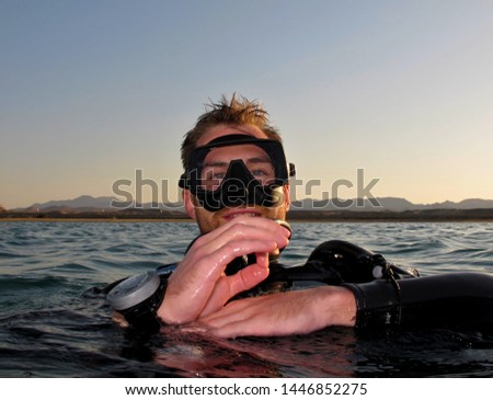 Scuba diver on the water surface, giving the ok sign with his hand.  Calm evening sea and smiling man in black diving neoprene suit with mask.