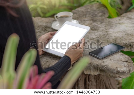 Mockup image of woman hands holding and using blank white screen  tablet computer pc with mobile smart phone and cup of coffee on the old wooden table at cafe outdoor.