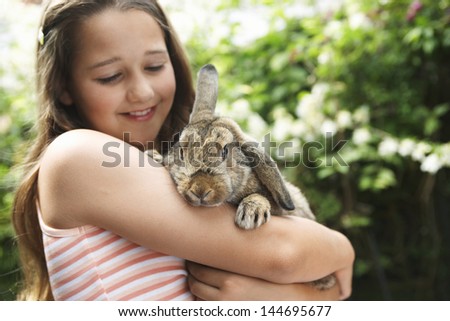 Happy young girl holding bunny rabbit in the backyard