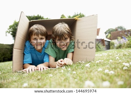 Portrait of two happy boys lying in cardboard box in the backyard Royalty-Free Stock Photo #144695974