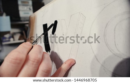 An artists hand with a paint brush painting retro letters and typography graphics. Artists hand painted signs and symbols. Studio art painting signage and letters.