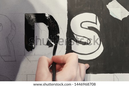 An artists hand with a paint brush painting retro letters and typography graphics. Artists hand painted signs and symbols. Studio art painting signage and letters.