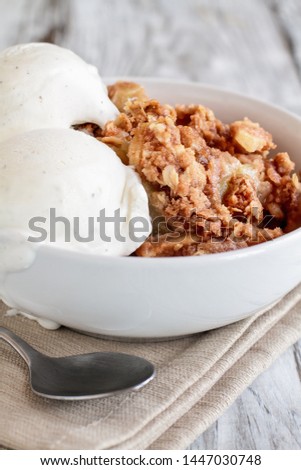 Fresh hot homemade apple crisp or crumble with crunchy streusel topping topped with vanilla bean ice cream. Selective focus with blurred background. 