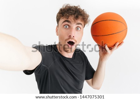 Photo closeup of excited young man in t-shirt wondering and taking selfie while holding basketball isolated over white background