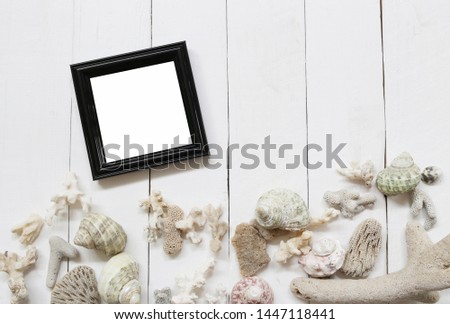 Black Wooden photo frame on a white wood floor and have Shells and coral reefs for Sea and summer tourism concept.