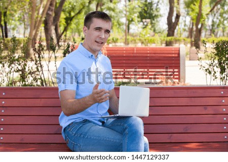 Young man with laptop sitting on a wooden bench. Portrait