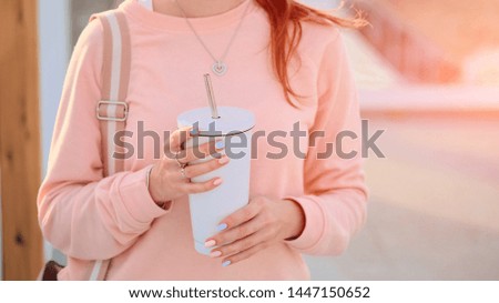 Close-up of young woman hands holding white thermo mug with tea or coffee. Cute girl with a thermos in hands. Zero waste concept.