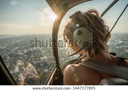 Portrait of beautiful blonde women enjoying helicopter flight. She is amazed by cityscape and wearing pilot headphones.
 Royalty-Free Stock Photo #1447177895