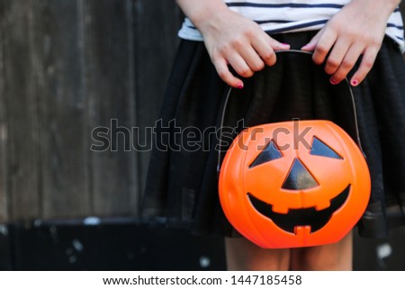 Smiling blond girl holding Halloween pumpkin jack o'lantern with sweet candy in hands on wooden background. Halloween celebration concept