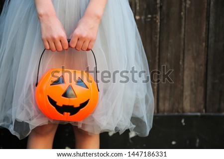 Smiling blond girl holding Halloween pumpkin jack o'lantern with sweet candy in hands on wooden background. Halloween celebration concept