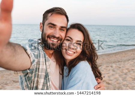 Beautiful young smiling couple spending time at the beach, embracing while taking a selfie
