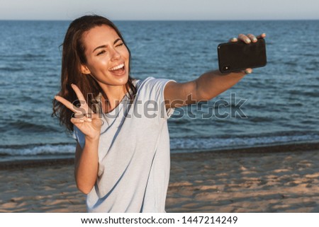 Beautiful young woman having a good time at the beach on a lovely day, taking a selfie