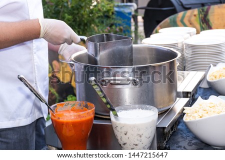 Chef preparing pasta boiling pasta and cooking. Boiled penne pasta without sauce in a white bowl during summer brunch outdoor setting in the garden. Food catering live cooking station during reception