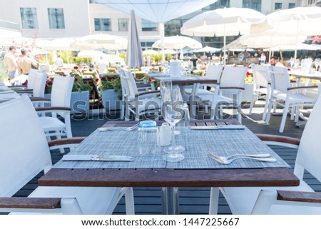 Table setting outdoor terrace. Nobody in the picture just table setup with cutlery and glasses. Pool with sun beds in the background. Blue and wood table, white chairs, summer time and sunshine
