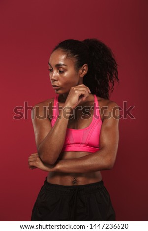 Picture of a concentrated strong young african fitness sports woman posing isolated over red wall background make stretching exercises.