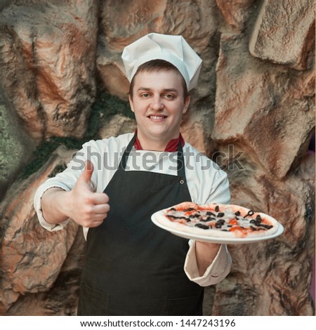 chef holds a big pizza and shows a thumb u