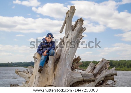 the boy sits on a branchy log by the river