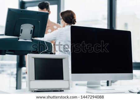 computer and monitor with blank screen and sportsman running on treadmill near doctor during endurance test