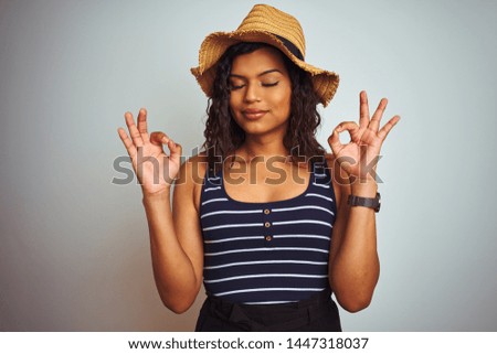 Beautiful transsexual transgender woman wearing summer hat over isolated white background relax and smiling with eyes closed doing meditation gesture with fingers. Yoga concept.