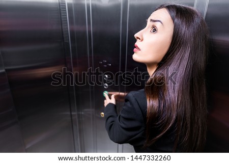 scared businesswoman, suffering from claustrophobia, looking up while pushing button in elevator Royalty-Free Stock Photo #1447332260