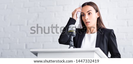 panoramic shot of worried lecturer suffering from fear of public speaking holding napkin near forehead while standing on podium tribune Royalty-Free Stock Photo #1447332419
