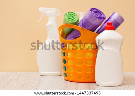 Plastic bottles of dishwashing liquid, basket with garbage bags, sponges on beige background. Washing and cleaning concept.