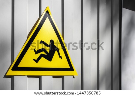 Yellow traffic sign warning for danger of falling on the gray fence, close-up. Fall danger or Slippery floor sign. falling man - sign of danger of falling because of construction and repair works
