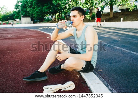 Young man sitting on the ground with a bottle of water after Jogging outdoors