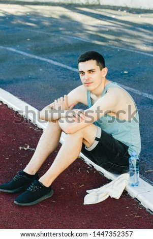 Young man sitting on the ground with a bottle of water after Jogging outdoors
