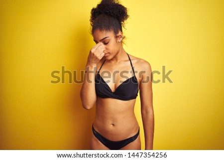 African american woman on vacation wearing bikini standing over isolated yellow background tired rubbing nose and eyes feeling fatigue and headache. Stress and frustration concept.