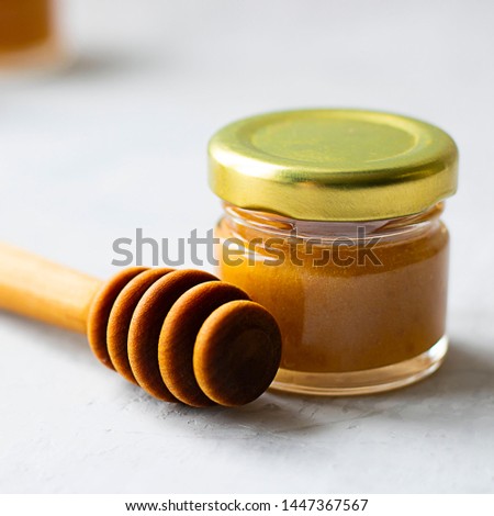 Close up Small glass jar of light yellow honey with metal cap and special wooden spoon isolate on grey cement background with copy space. Healthy product, natural, Square. Selective focus