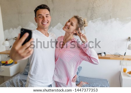 young couple having fun in bedroom in morning, man and woman making selfie photo on smart phone camera, smiling happy, family living together, wearing pajamas