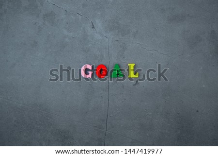 The multicolored goal word is made of wooden letters on a grey plastered wall background.