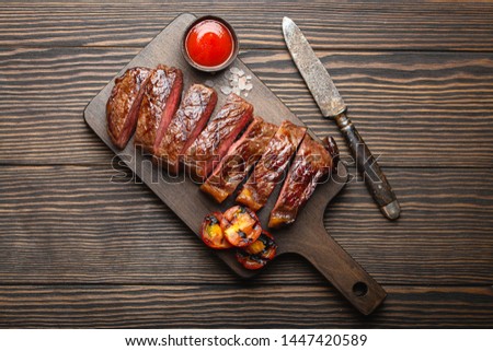 Grilled or fried and sliced marbled meat steak, tomatoes as a side dish and sauce on wooden cutting board, top view, close-up, wooden rustic background. Beef meat steak sirloin concept 