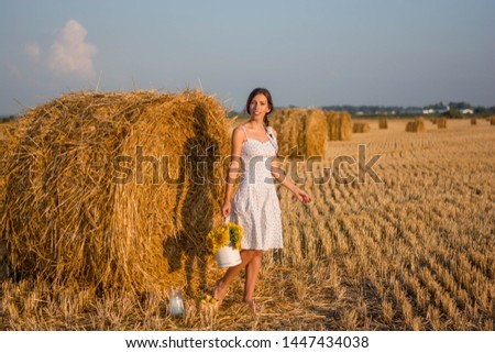 woman in a barefoot sundress with a bouquet of sunflowers on the background of hay
