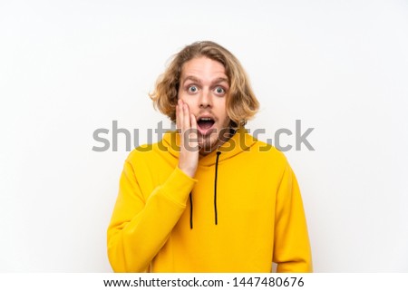 Blonde man with  sweatshirt over white wall with surprise and shocked facial expression
