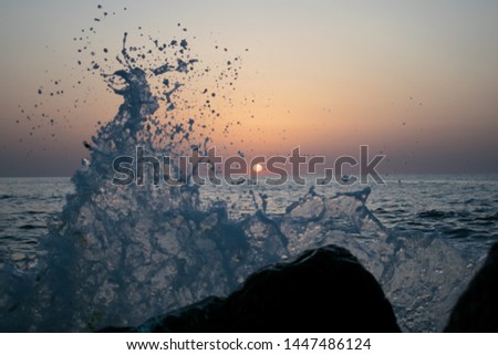 Waves crash against a rocky shoreline . a beautiful sunrise on the ocean. rocks near the shore. waves that hit the stones and water is scattered