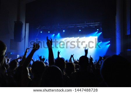 A crowd of people dancing at a musical rock concert under the light and smoke of spotlights