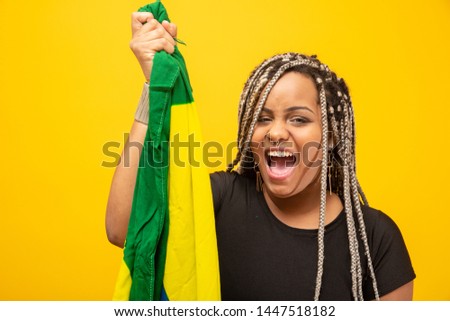 Afro girl cheering for favorite brazilian team, holding national flag in yellow background.