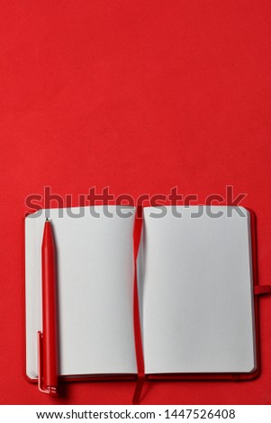 Notebook for notes in the red cover. With a red bookmark and pen. Lies opened on a coral background. School supplies.