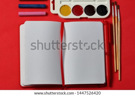 Accessories for drawing and sketching. Decomposed on the surface of coral color. In the middle of the open notebook. School supplies.