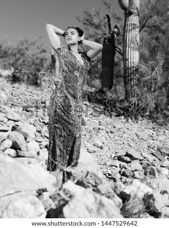 Powerful confident woman posing in front of desert scene with cactus in the background. Snake print dress. Model with dark skin. Black and white photograph.