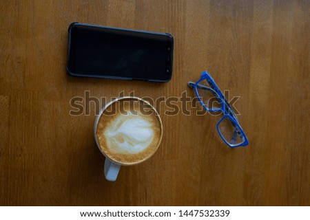 Workspace with laptop, a cup of coffee and a mouse for a laptop, phone, glasses on a white wooden table. Gray laptop, blue mouse for working at a computer, blue glasses for vision, cappuccino.