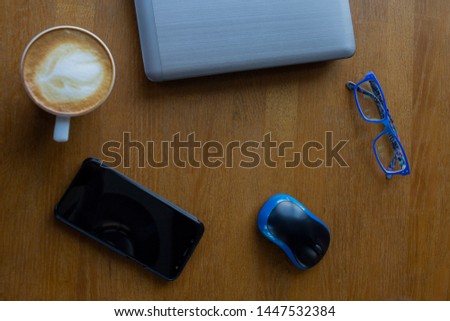 Workspace with laptop, a cup of coffee and a mouse for a laptop, phone, glasses on a white wooden table. Gray laptop, blue mouse for working at a computer, blue glasses for vision, cappuccino.