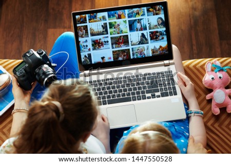 modern mother and child sitting on sofa in the modern living room viewing image library while transferring photos from DSLR photo camera on a laptop.