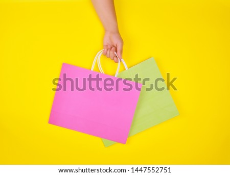hand holding two paper shopping bags on a yellow background, concept of seasonal sales