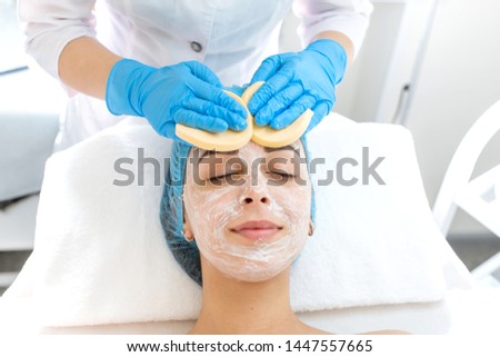 The beautician massages the patient's face with the sponges. A young girl is undergoing a course of spa treatments in the office of a beautician. Moisturizing, cleaning and facial skin care. procedure