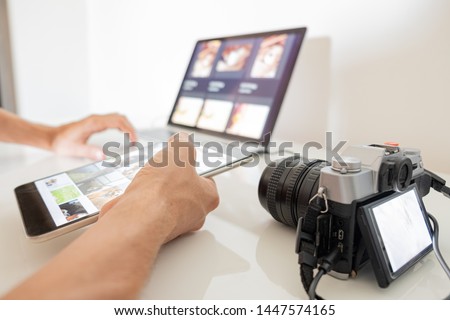 Managing digital images on a computer. Human hands hold a tablet to organise or import images from camera to laptop