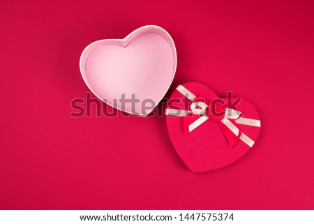 open red heart-shaped gift box with a bow on a red background, top view, festive backdrop